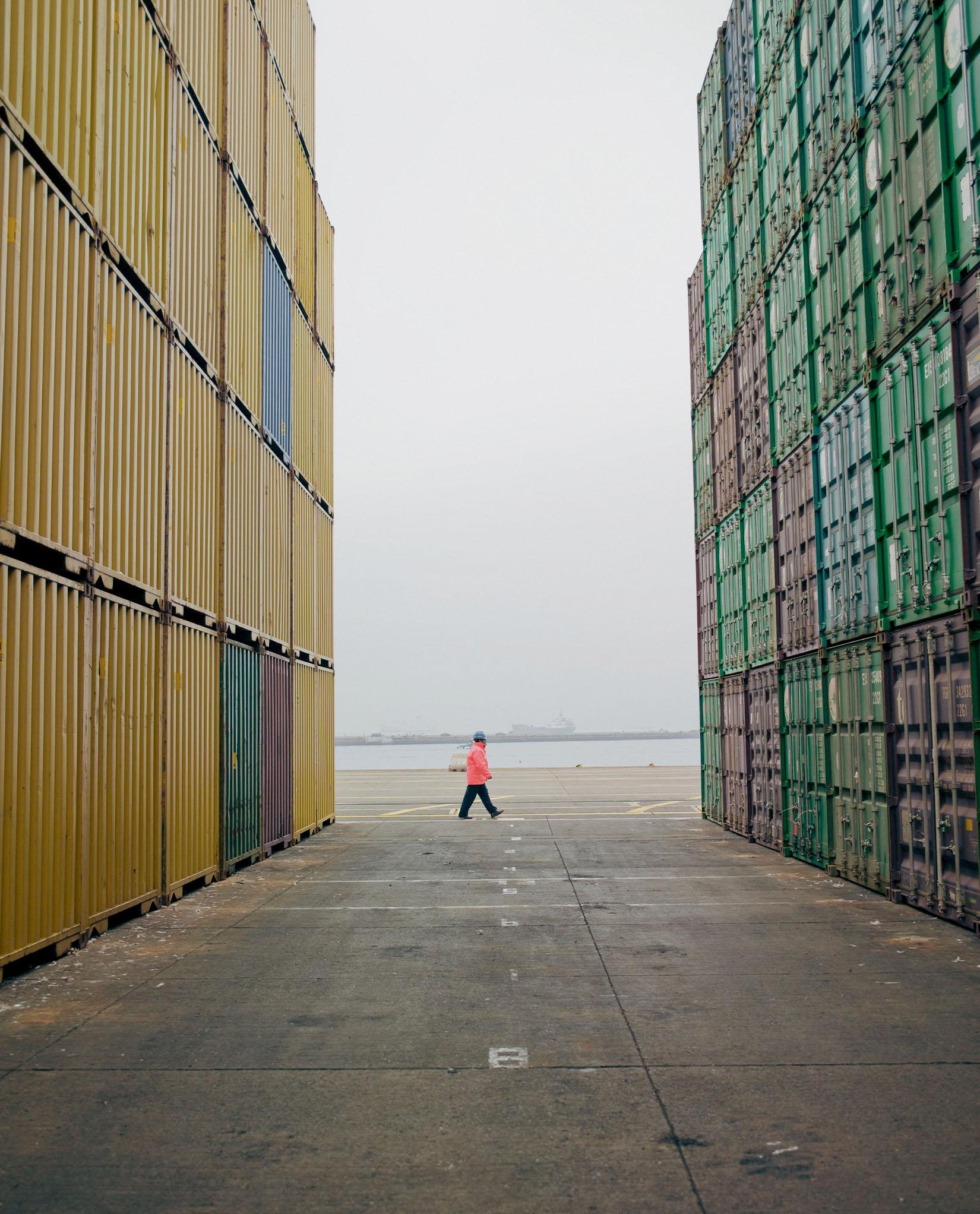 Person standing between containers in a shipping yard.